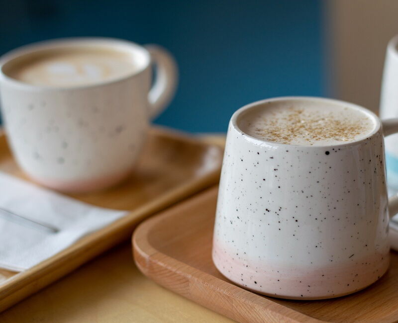 Zwei Keramiktassen mit Kaffee auf Holztabletts, eine mit Schaum und Gewürzen. Bilddatei: dummy.jpg.